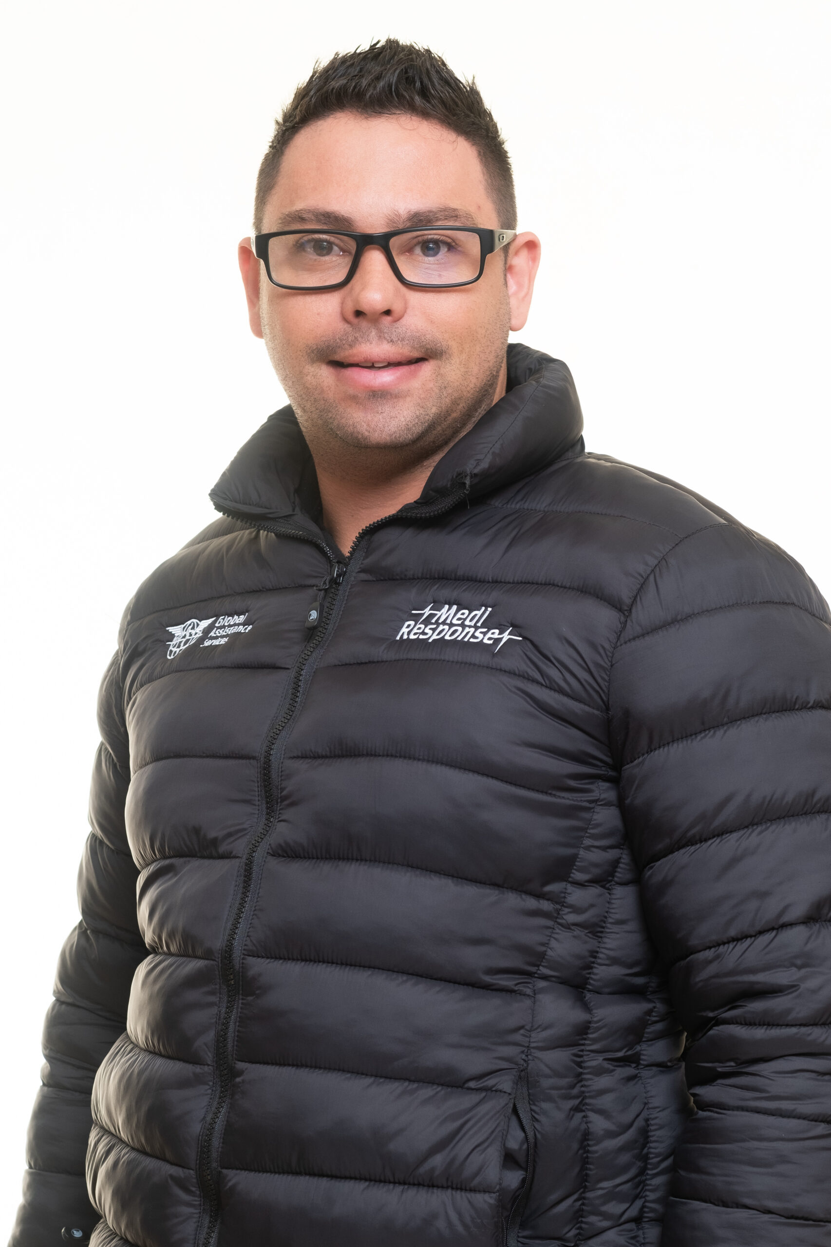A Medi Response emergency medical services team member in a black puffer jacket, smiling against a white studio background.