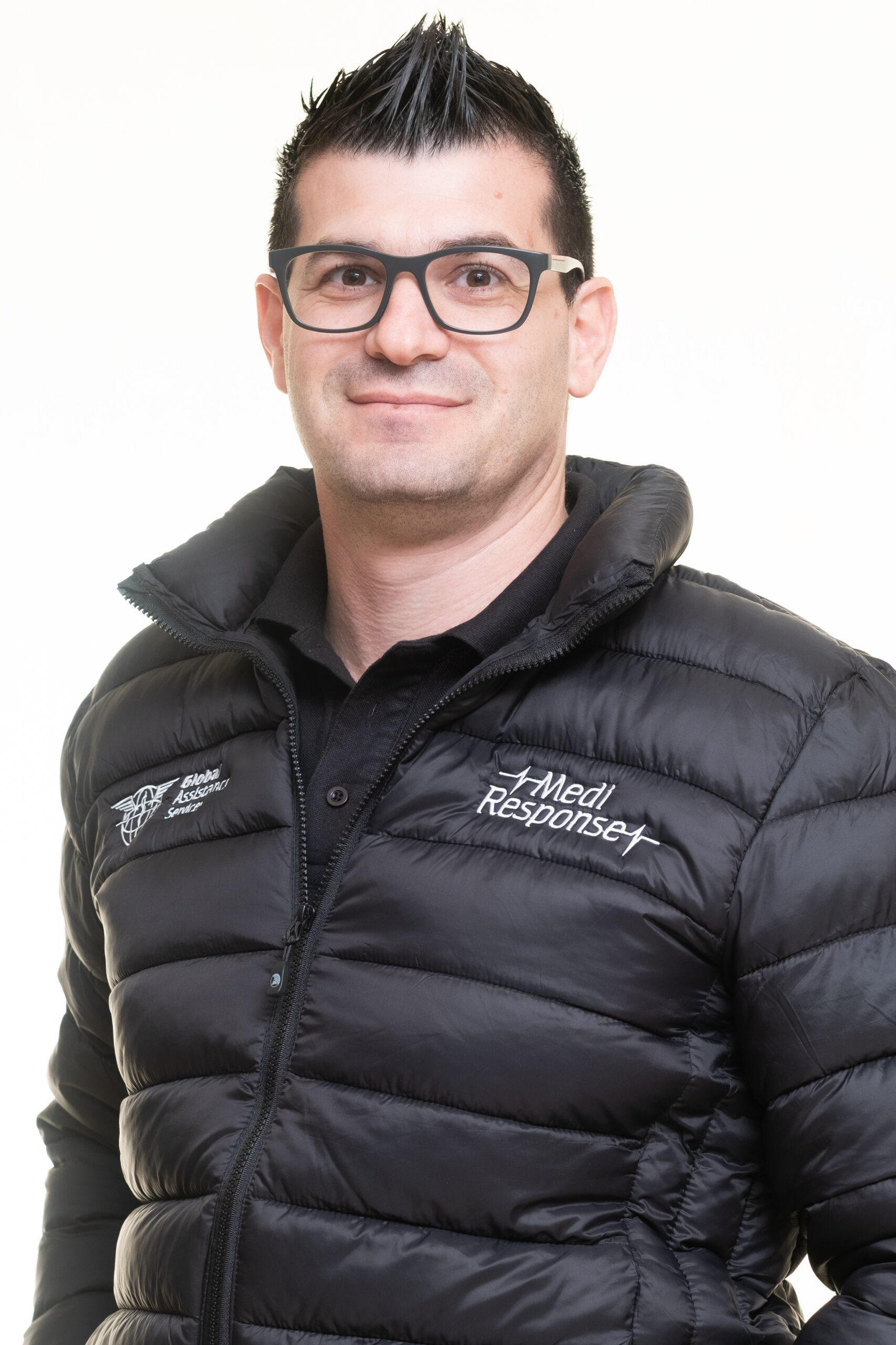 Medi Response emergency medical care team member with glasses in a branded puffer jacket against a light background.